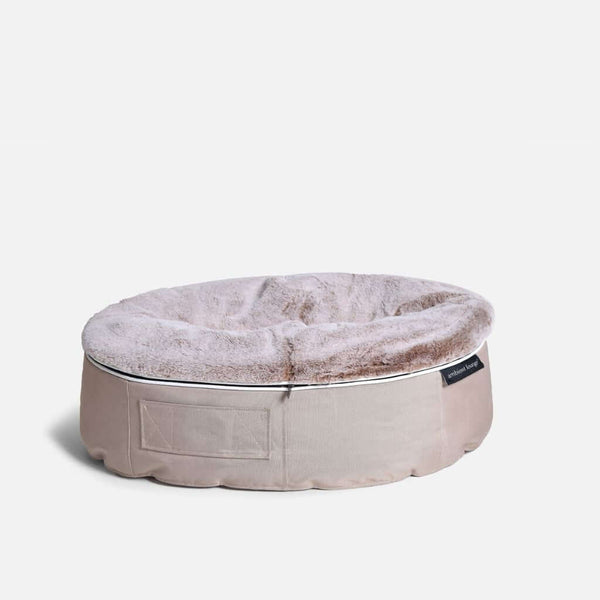 Hringlaga, beige hundeseng Sandstorm Cappuccino frá Ambient Lounge með mjúkum, ljósbrúnum toppi og efnismiða á hliðinni, á hvítum bakgrunni.